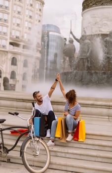Portrait of cheerful Caucasian young couple man and woman holding many paper bags after shopping while walking and talking on street. Happy family couple with packages outdoor. Buying concept photo