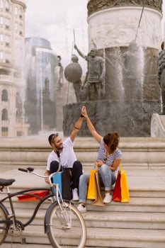 Portrait of cheerful Caucasian young couple man and woman holding many paper bags after shopping while walking and talking on street. Happy family couple with packages outdoor. Buying concept photo