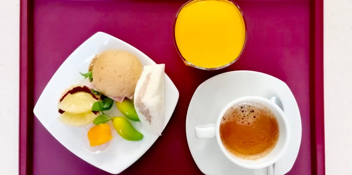 top view photo of a breakfast set in a dark purple tray with sweets, orange juice and hot coffee