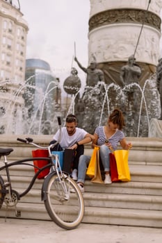 Portrait of cheerful Caucasian young couple man and woman holding many paper bags after shopping while walking and talking on street. Happy family couple with packages outdoor. Buying concept photo