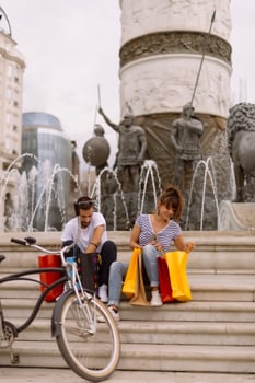 Portrait of cheerful Caucasian young couple man and woman holding many paper bags after shopping while walking and talking on street. Happy family couple with packages outdoor. Buying concept photo