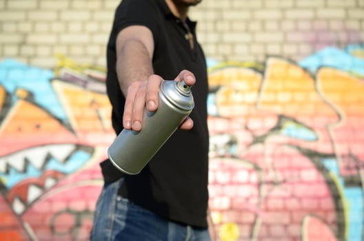 Young graffiti artist aims his spray can on background of colorful graffiti in pink tones on brick wall. Street art and contemporary painting process photo