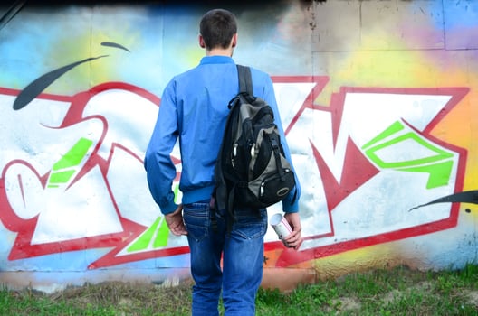 A young graffiti artist with a black bag looks at the wall with his graffiti on a wall. Street art concept photo