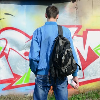 A young graffiti artist with a black bag looks at the wall with his graffiti on a wall. Street art concept photo