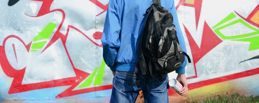 A young graffiti artist with a black bag looks at the wall with his graffiti on a wall. Street art concept photo