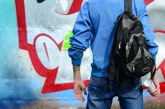 A young graffiti artist with a black bag looks at the wall with his graffiti on a wall. Street art concept photo