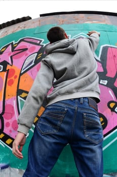 A young guy in a gray hoodie paints graffiti in pink and green c photo