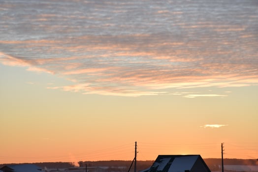 Sunset landscape in the countryside in winter. The setting sun behind the roof of the house in the evening. The disk of the sun and the evening sunset. Yellow pink beautiful sunset and sky. photo