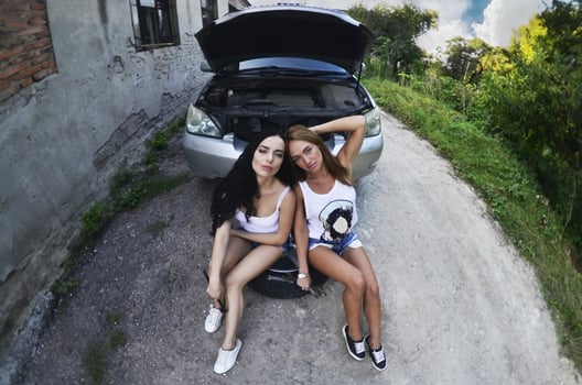 Two young and sexy girls with wheel wrenches around a silvery ca photo