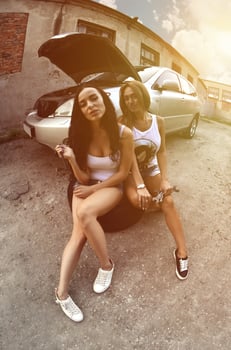 Two young and sexy girls with wheel wrenches around a silvery ca photo