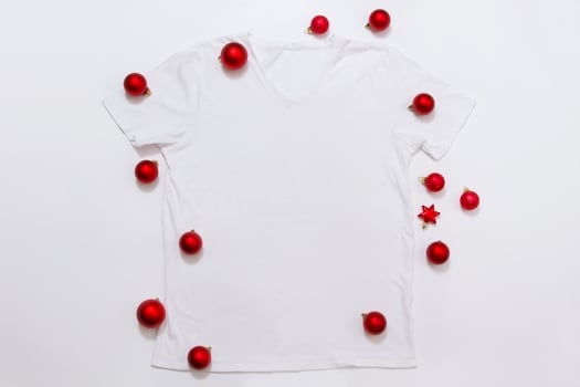 Close up white blank template t shirt with copy space and Christmas Holiday concept. Top view mockup t-shirt and red holidays decorations on white background. Happy New Year accessories. Xmas outfit photo