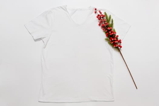 Close up white blank template t shirt with copy space and Christmas Holiday concept. Top view mockup t-shirt and red holidays decorations on white background. Happy New Year accessories. Xmas outfit photo