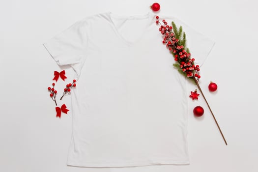 Close up white blank template t shirt with copy space and Christmas Holiday concept. Top view mockup t-shirt and red holidays decorations on white background. Happy New Year accessories. Xmas outfit photo