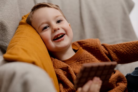 Little adorable boy sitting on the couch at home and eating chocolate bar. Child and sweets, sugar confectionery. Kid enjoy a delicious dessert. Preschool child with casual clothing. Positive emotion. photo