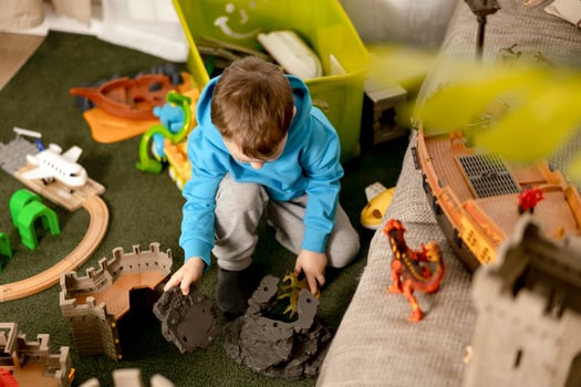 Little caucasian boy with blue hoodie playing with colourful toys at home. Child having fun. Happy and cheerful kid plays with ship, dinosaurs, castle. Leisure activity, domestic life. Cozy room. photo