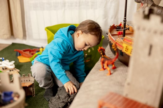 Little caucasian boy with blue hoodie playing with colourful toys at home. Child having fun. Happy and cheerful kid plays with ship, dinosaurs, castle. Leisure activity, domestic life. Cozy room. photo