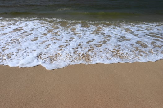 Ocean shore with sandy beach and advancing wave.  Water foam with smooth sand.  Beautiful waves on the sand beach background. photo