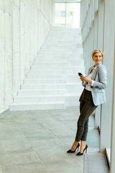 Businesswoman using mobile phone on modern office hallway photo