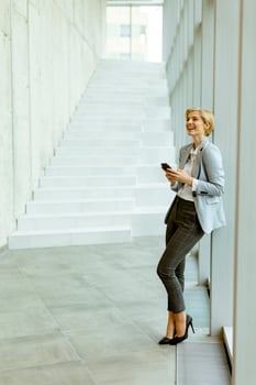 Businesswoman using mobile phone on modern office hallway photo