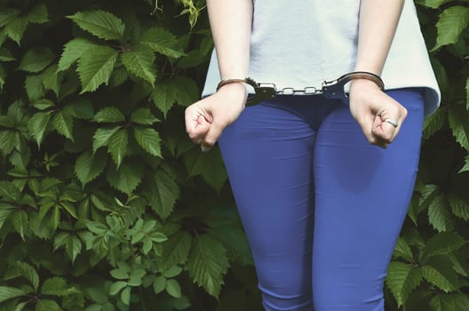 Fragment of a young criminal girl's body with hands in handcuffs against a green blossoming ivy leaves background. The concept of detaining an offender of a female criminal in a rural environment photo