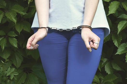 Fragment of a young criminal girl's body with hands in handcuffs against a green blossoming ivy leaves background. The concept of detaining an offender of a female criminal in a rural environment photo