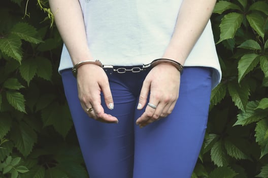 Fragment of a young criminal girl's body with hands in handcuffs against a green blossoming ivy leaves background. The concept of detaining an offender of a female criminal in a rural environment photo