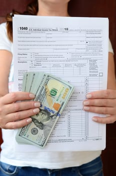 The girl holds in her hands the tax form and a large number of dollar bills photo