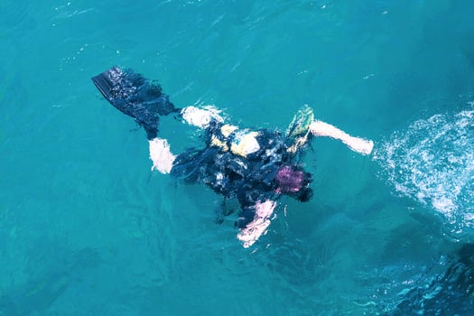 Top view of scuba diver swimming under water and examines the seabed. Scuba diver bubbles coming from bottom to surface. photo