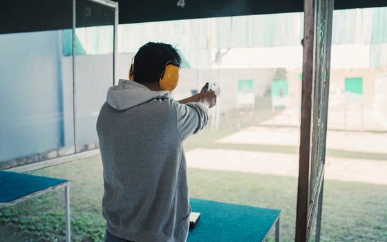 Asian shooter man wearing noise canceling headphones and black clothes practicing shooting short gun at the shooting range. Shooting sports for meditation and self-defense, recreational activities. photo