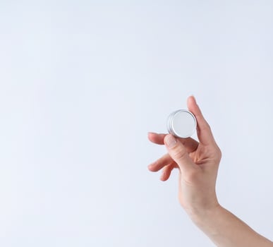 Woman hand holding blank round tin container for lip balm or cream on light gray background photo