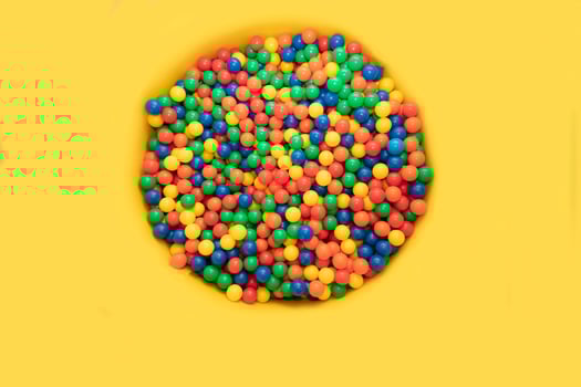 On a yellow background, a spot of multi-colored plastic balls. photo