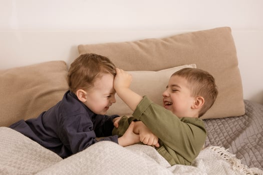 Two little and cute caucasian boys playing together on the bed at home. Interior and clothes in natural earth colors. Cozy environment. Children having fun, two brothers kittle each other. photo