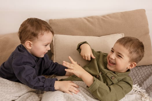 Two little and cute caucasian boys playing together on the bed at home. Interior and clothes in natural earth colors. Cozy environment. Children having fun, two brothers kittle each other. photo