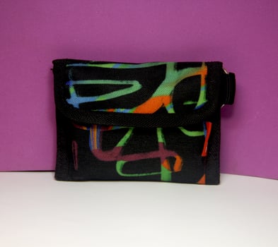 Black canvas fabric wallet with colorful doodle pattern for young or teen who love artsy things. Savings financial themed object photo isolated on white and purple background surface.