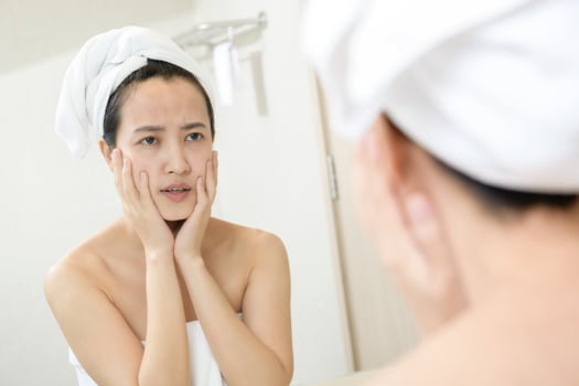 Problem skin. Concerned young asian women popping pimple on cheek while standing near mirror in bathroom. young asian women with acne photo