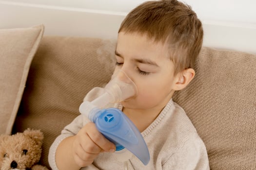 Sick little boy with inhaler for cough treatment. Unwell kid doing inhalation on his bed. Flu season. Medical procedure at home. Interior and clothes in natural earth colors. Cozy environment. photo