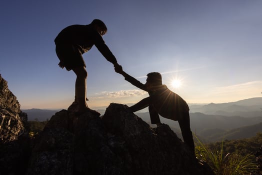 Silhouette of helping hand between two climber.  couple hiking help each other silhouette in mountains with sunlight. The men helping pull people up from high cliffs photo