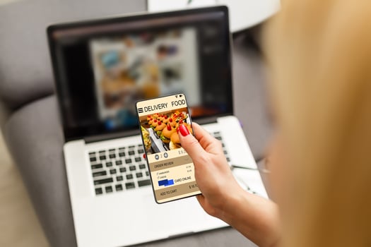 Woman using laptop and smartphone in cafe holding phone with app delivery food screen photo