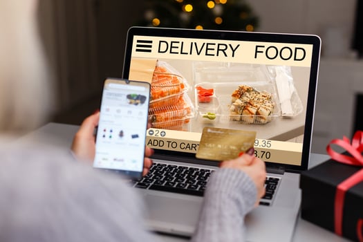 Woman using laptop and smartphone in cafe holding phone with app delivery food screen photo