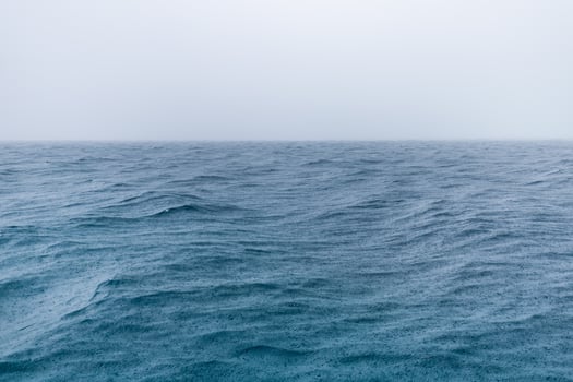 Rain over the stormy sea, blue ocean water and rain drops. Endless sea view horizon, fog and misty relaxing mood. Abstract seaside photo