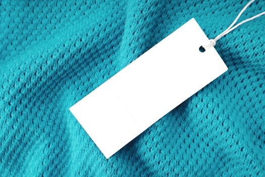 White rectangular clothing tag on turquoise knitted fabric background. Shopping, sale, discount photo