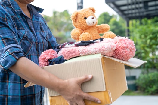 Holding clothing donation box with used clothes and doll at home to support help for poor people in the world. photo