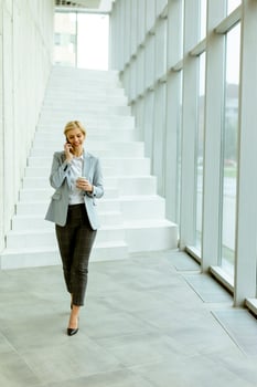 Businesswoman using mobile phone on modern office hallway photo