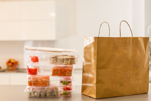 Sushi rolls in plastic box near paper package on white table. Delivery. Take away. photo
