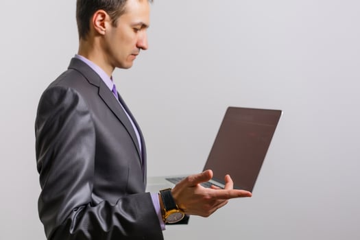 Working with joy. Handsome young man using his laptop and looking at camera with smile while standing against white background photo