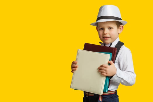 Happy smiling boy in glasses with thumb up is going to school for the first time. Child with school bag and book. Kid indoors of the class room with blackboard on a background. Back to school. photo