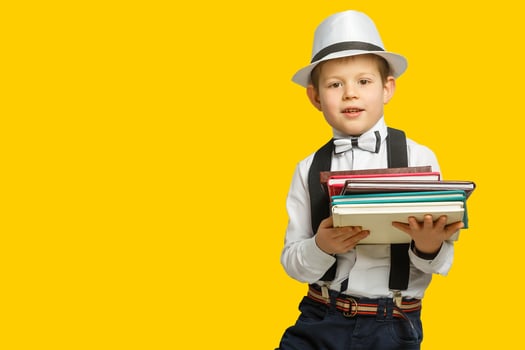 Happy smiling boy in glasses with thumb up is going to school for the first time. Child with school bag and book. Kid indoors of the class room with blackboard on a background. Back to school. photo