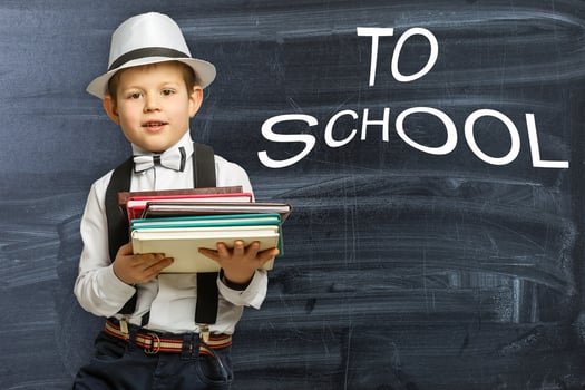 Back to school. Funny little boy in glasses pointing up on black photo