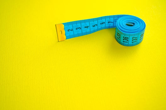 Measuring tape with copy space for text. Blue measuring tape on bright yellow background. photo
