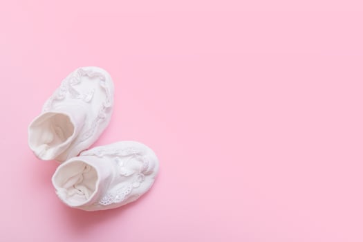 white booties for a newborn on a pink background with copy space photo